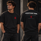 Lifestyle concept of a male model showing both sides of the DISAPPOINT THEM. heavyweight black T-shirt