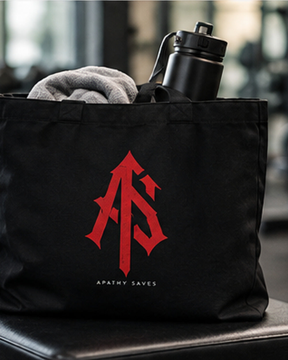 Styled lifestyle mockup of the black ApathySaves tote beside workout clothes and a water bottle