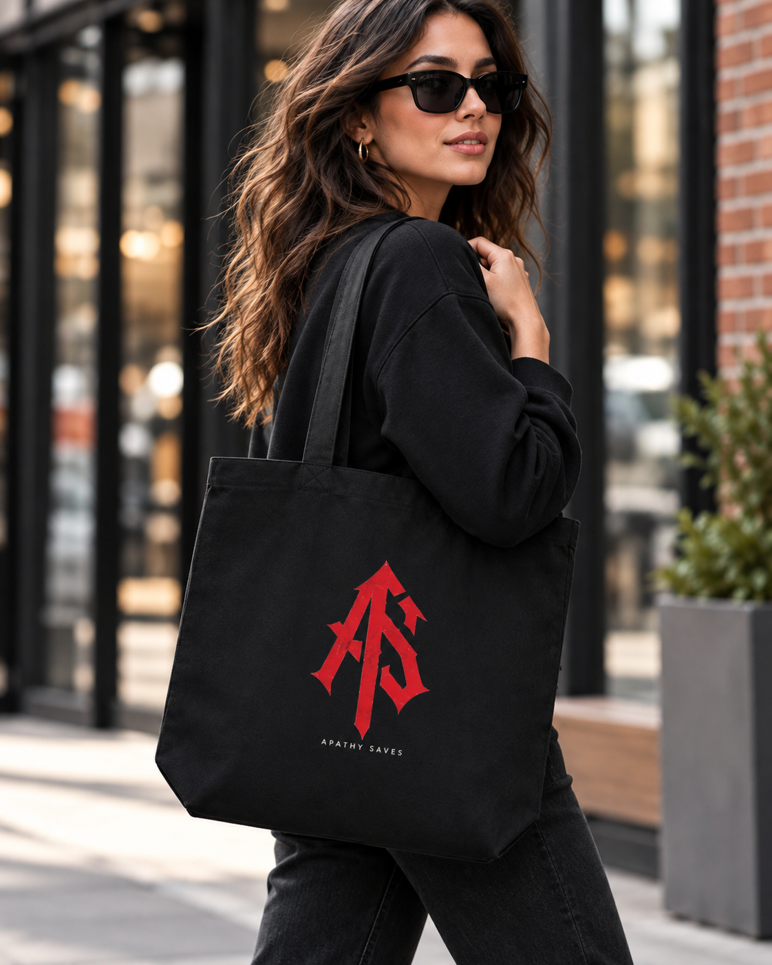 Styled lifestyle mockup of woman in black streetwear carrying ApathySaves black eco tote with centered red AS monogram and small APATHY SAVES lettering