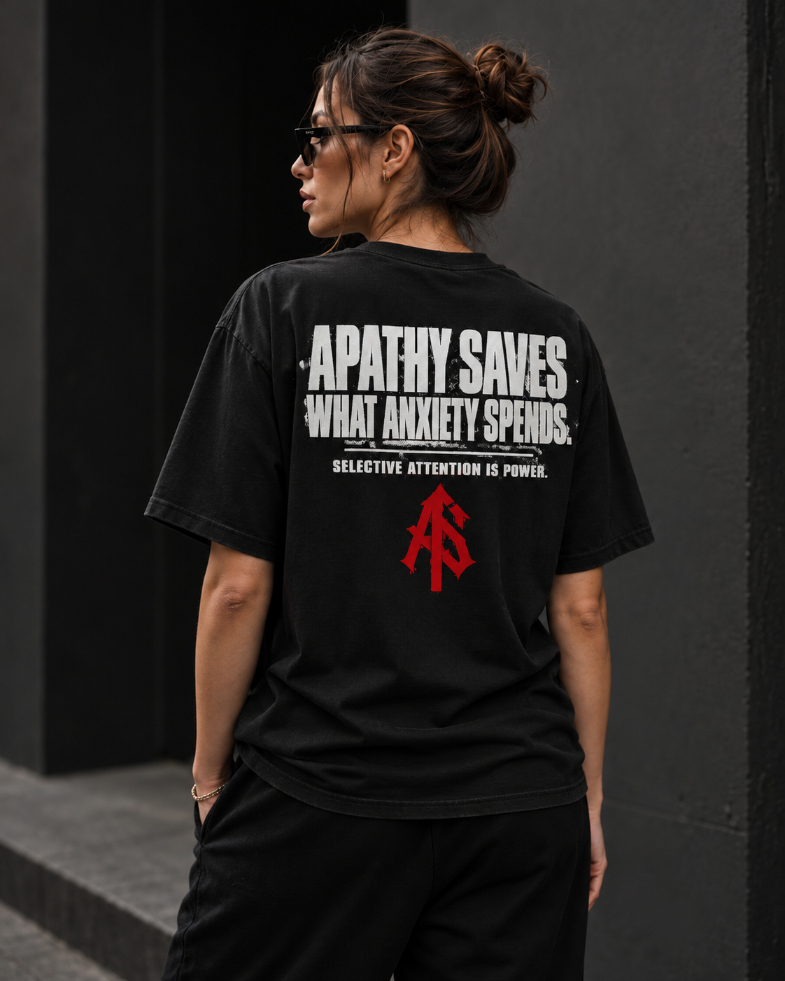 Woman wearing ApathySaves black heavyweight tee with Apathy Saves What Anxiety Spends back graphic and red AS logo